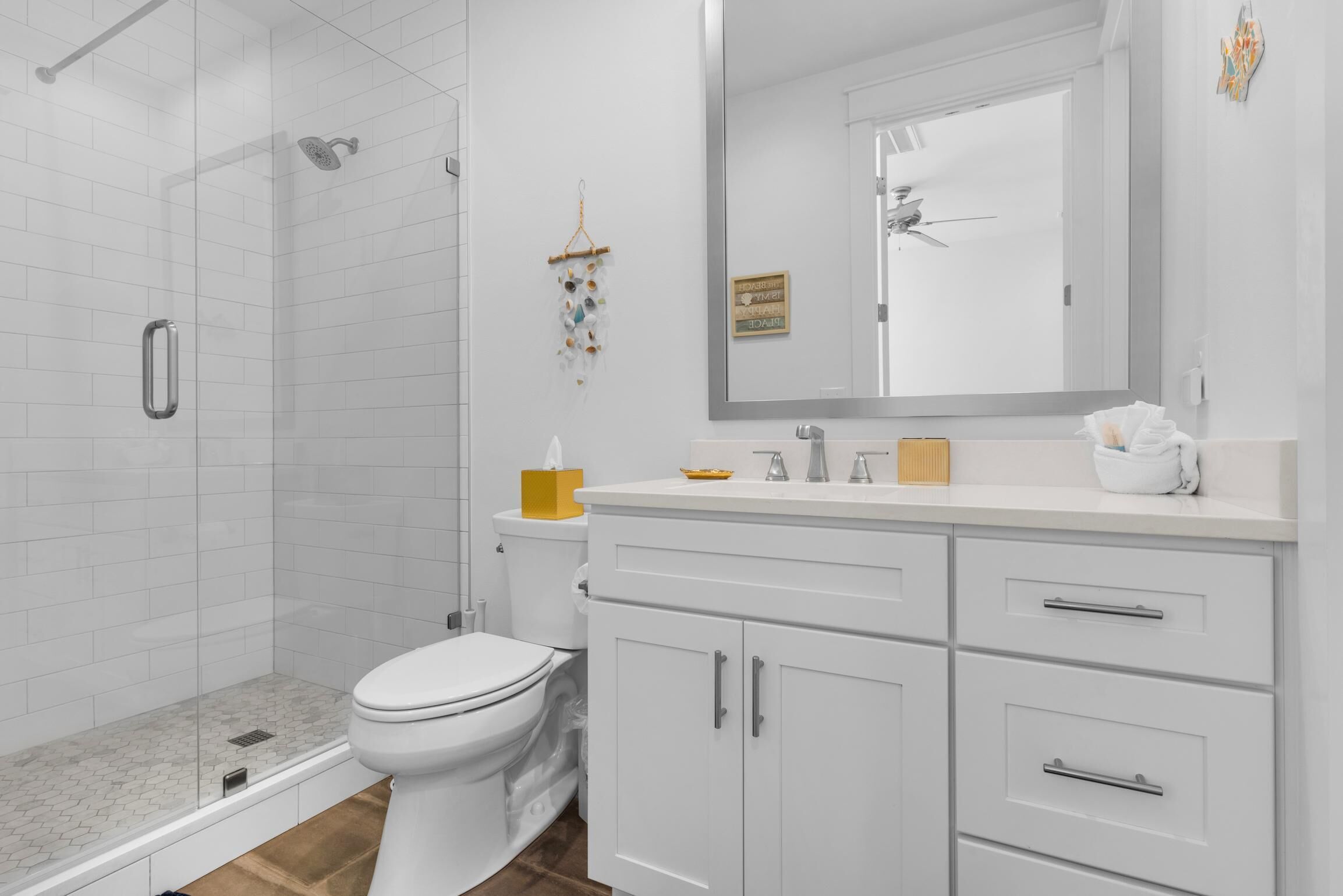 A modern bathroom with a glass shower enclosure, a toilet, a vanity with drawers, and a large mirror.
