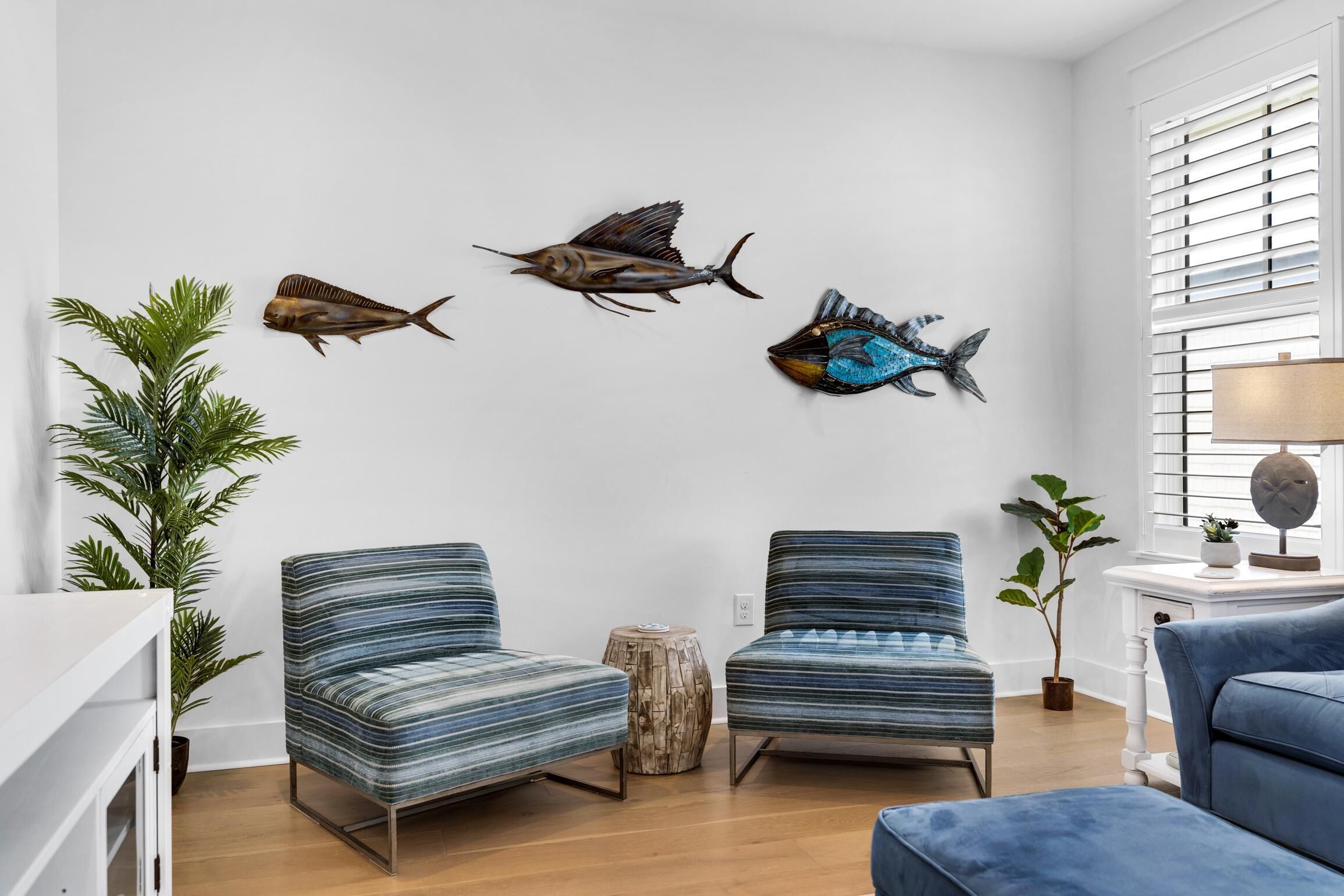 A living room with two striped armchairs, a coffee table, and three wall-mounted fish decorations.