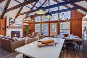 Un salon spacieux doté d’une cheminée, d’un canapé en cuir, d’un coin repas et de grandes fenêtres.