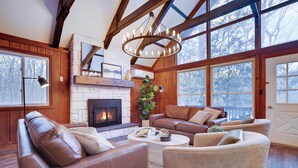 Ein großzügiges Wohnzimmer mit Ledersofas, einem Kamin und großen Fenstern.