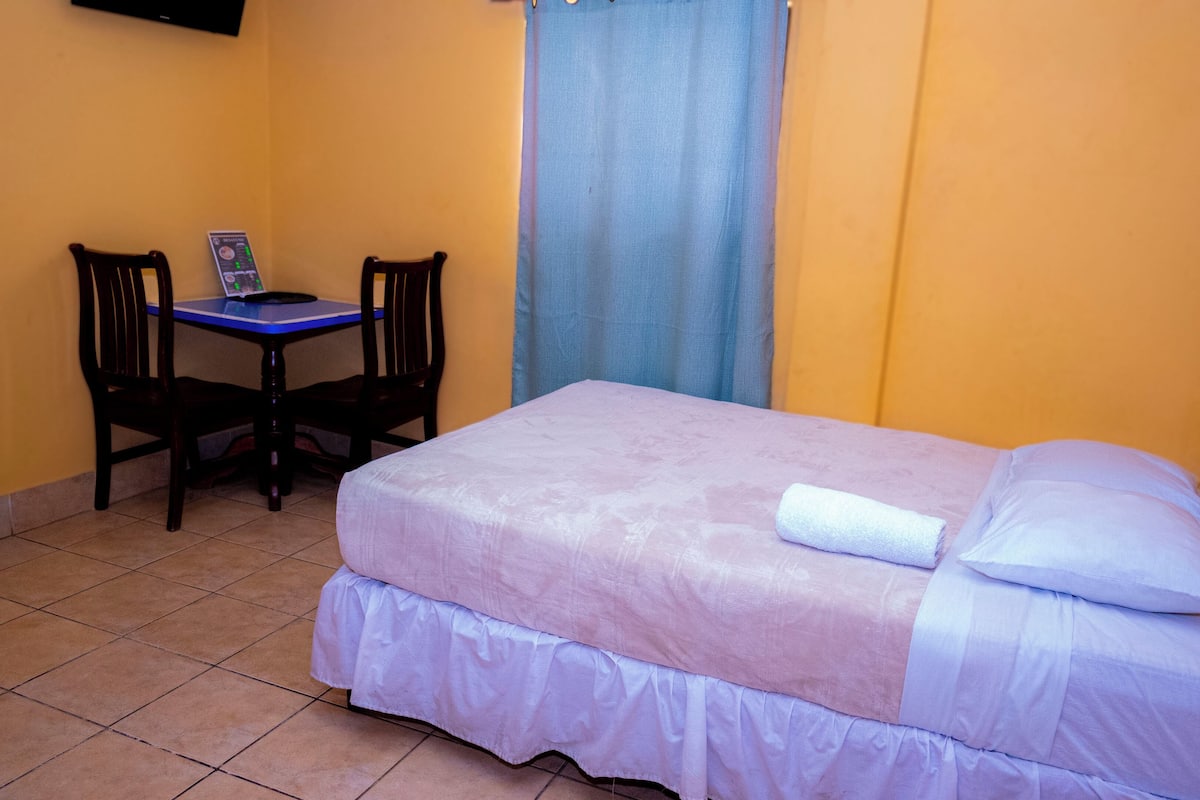 A small room with a bed, a desk, two chairs, and a curtain.