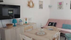 A cozy living room with a flat-screen TV, a wooden dining table, a pink sofa, and a teal armchair. - Mini villa with private garden - Residence with swimming pool Lecci near Porto-Vecchio (Lecci)