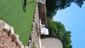 A patio area with white plastic chairs and a table, surrounded by a stone wall and a grassy lawn. - Mini villa with private garden - Residence with swimming pool Lecci near Porto-Vecchio (Lecci)