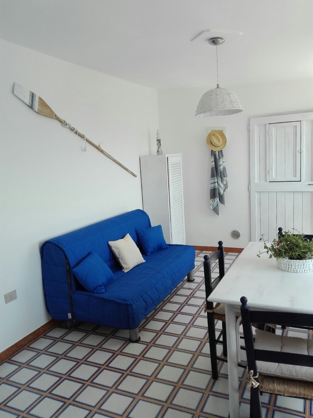 A room with a blue sofa, a white table with a plant, a white wardrobe, and a patterned floor.