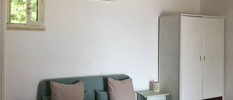 A room with a teal sofa, a white wardrobe, and a small white table with a decorative item.
