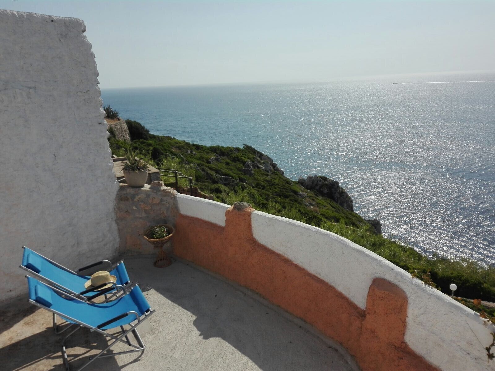 Ein Balkon mit blauem Stuhl und Blumentöpfen mit Blick auf die Küste.