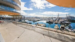 Un puerto deportivo con numerosas embarcaciones amarradas, un edificio moderno de fachada curva y un cielo despejado.