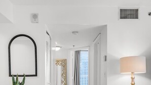 A hallway with a white floor, a decorative mirror, a plant, a lamp, and a view into another room.