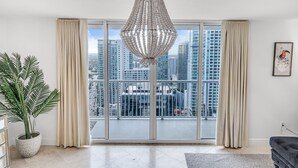 A spacious living room with a large sliding glass door leading to a balcony, a tall decorative chandelier, and a potted plant.