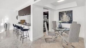 A modern kitchen with a central island, bar stools, and a dining table with chairs.