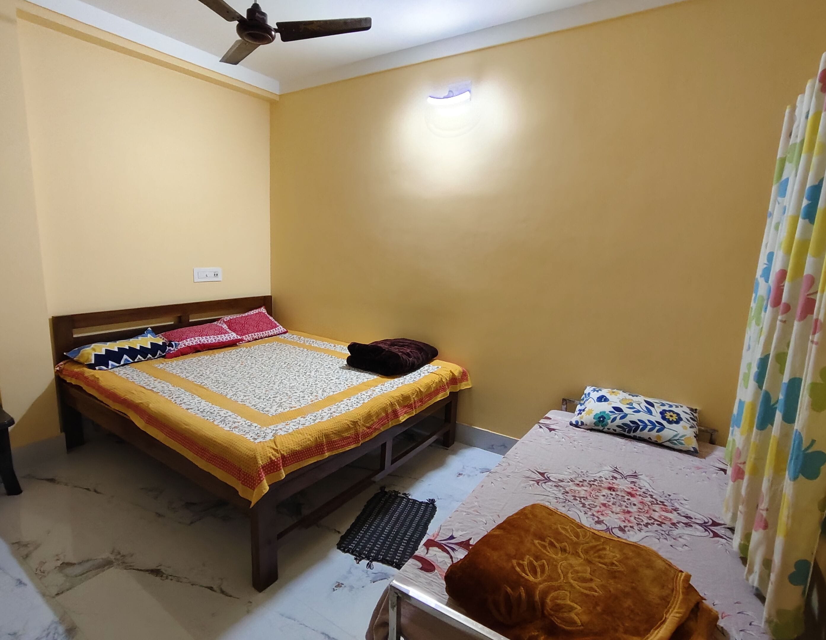 A bedroom with a bed, a desk, a ceiling fan, and a window with curtains.