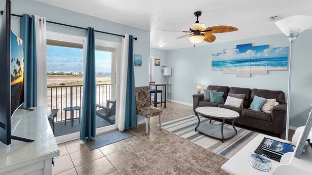 A living room with a sofa, a coffee table, a TV, and a balcony with curtains. - Sunset Suite (Navarre)