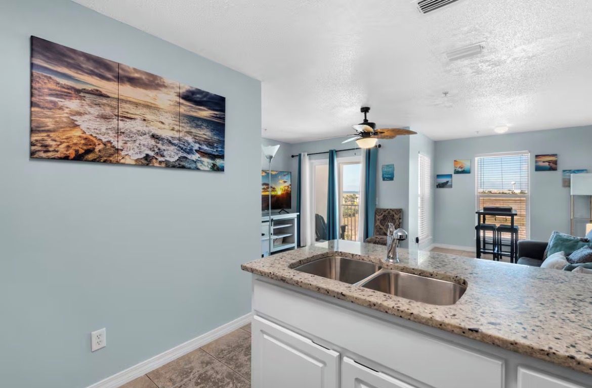 A kitchen with a granite countertop, a double sink, and a ceiling fan.
