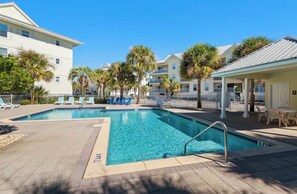 A swimming pool with a clear blue water, surrounded by palm trees and a white building.
