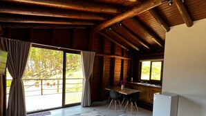 Une chambre spacieuse avec un grand lit, un bureau et un réfrigérateur. Les fenêtres offrent une vue sur une forêt.