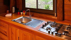 Une cuisine rustique aménagée dans une cabane en bois, avec une grande fenêtre, un évier et une cuisinière à gaz.