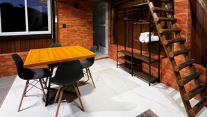 Un intérieur rustique avec une table et des chaises en bois, un espace de couchage en mezzanine, un escalier en bois et un mur en briques.