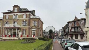 Een straat met geparkeerde auto's, een gebouw met een balkon en een verzorgd gazon.