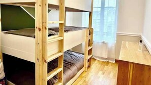 Een slaapkamer met stapelbed, houten vloer en een raam met gordijnen.