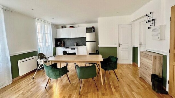 Een kleine keuken met witte kasten, een houten eettafel en vier groene stoelen.