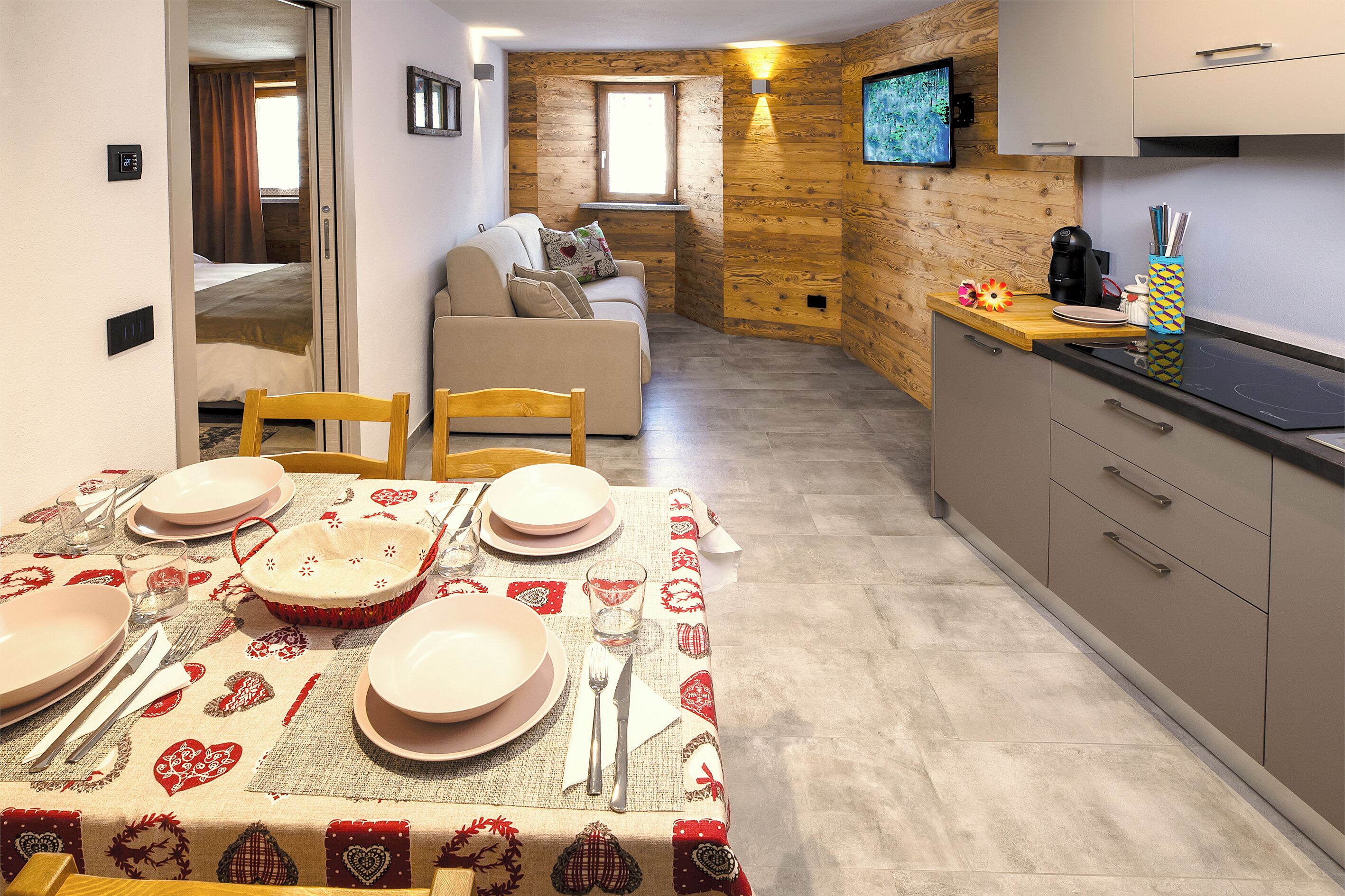 A modern kitchen with wooden accents, a dining area with a table set for four, and a cozy living space with a sofa and a TV.