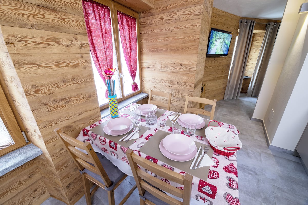 A dining area with a wooden interior, a table set for four, and a TV mounted on the wall.