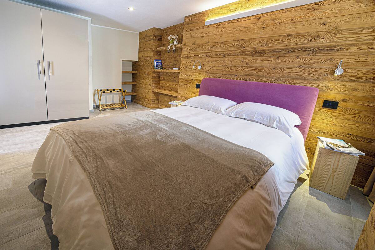 A bedroom with a bed, wooden wall paneling, a wardrobe, and a small wooden nightstand.