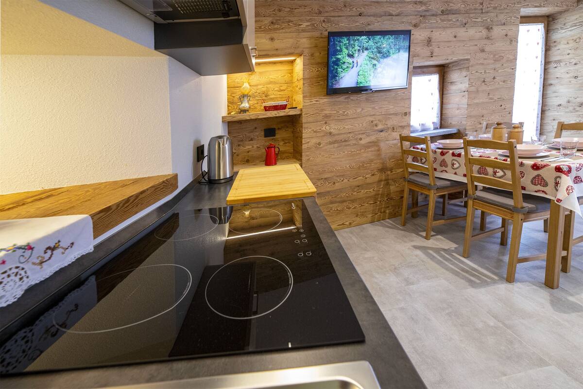 A modern kitchen with a black stove, wooden cabinets, and a dining area with a table and chairs.