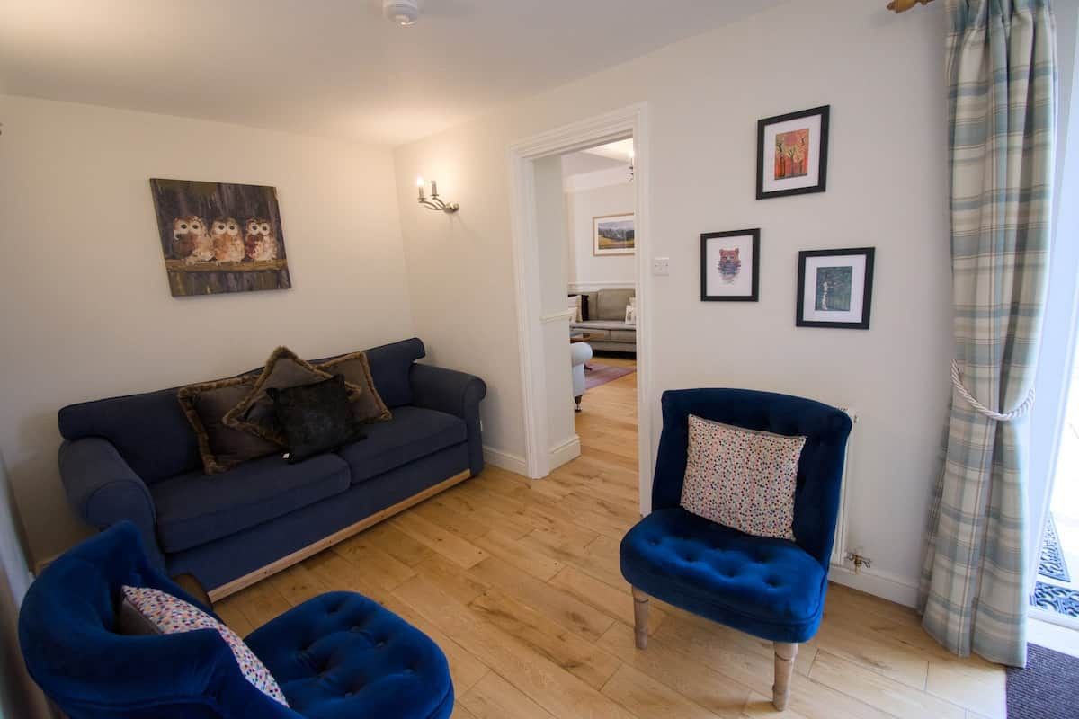 A living room with a dark blue sofa, a blue armchair, and a blue bean bag chair. There are framed pictures on the wall and a door leading to another room.