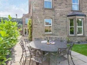 A stone building with a round outdoor table and chairs, surrounded by a well-maintained lawn. - Haddon Villa | Central Bakewell | Sleeps 12 (Bakewell)