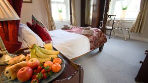 Ein Hotelzimmer mit Bett, Nachttisch mit Früchten und Brot, Lampe und Blick ins Freie.