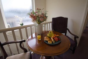 A dining table with a plate of fruit, a glass of orange juice, and a vase of flowers.