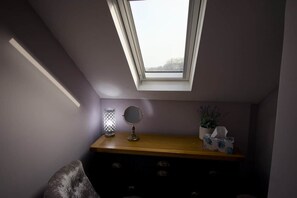 Ett rum med ett takfönster, en byrå i trä, en lampa, en spegel och en växt.