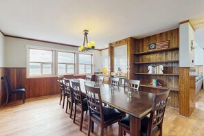 A dining area with a wooden table and chairs, a chandelier, and a bookshelf with books.