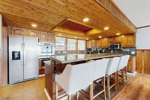 A kitchen with wooden cabinets, a stainless steel refrigerator, an oven, a microwave, and a bar area with stools.
