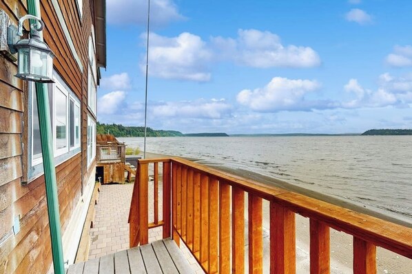 A wooden deck with a railing overlooking a body of water, a brick pathway, and a wooden building with windows and a lantern.