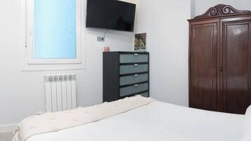Un dormitorio con una cama, un aparador, un televisor montado en la pared y un radiador.
