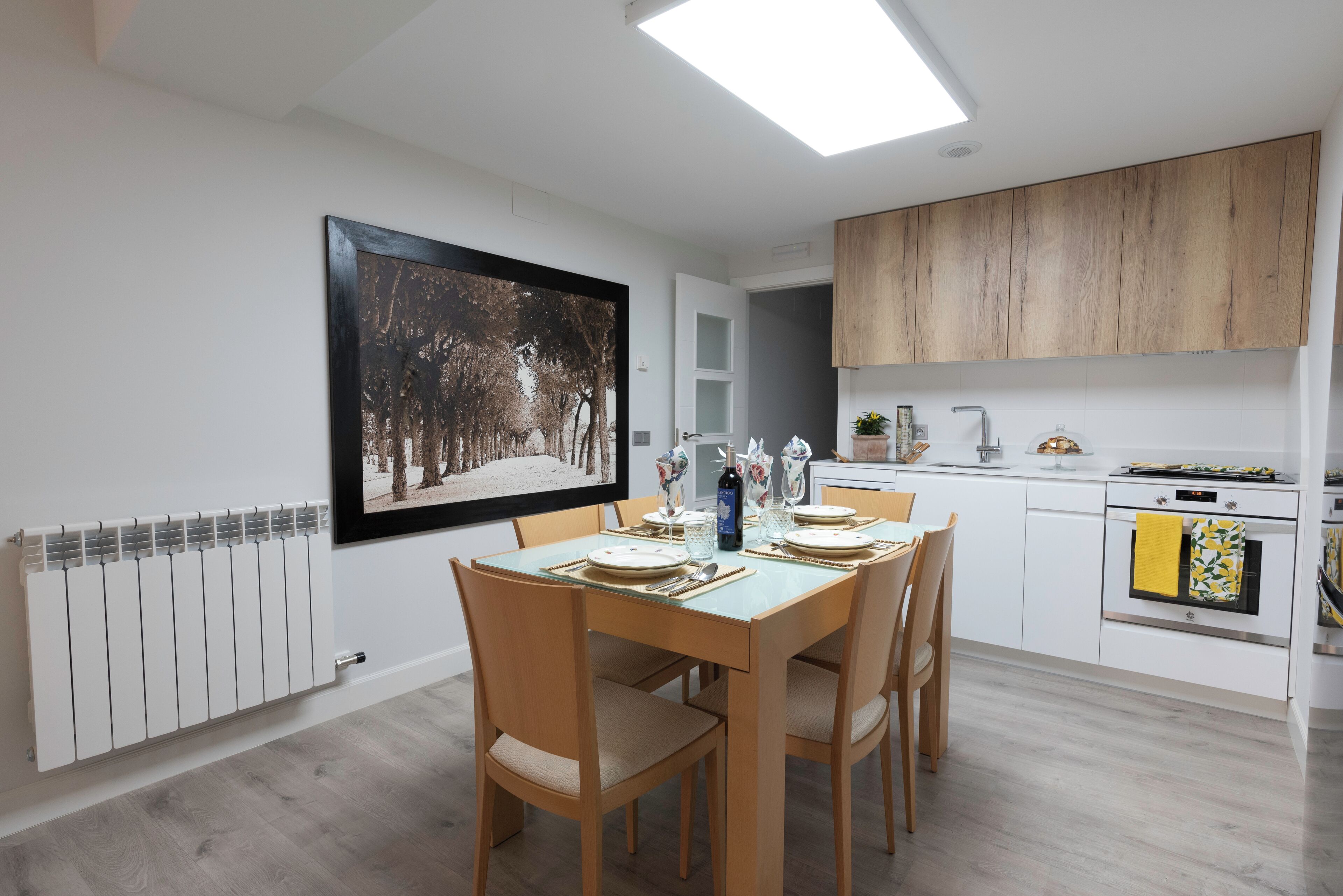 A modern kitchen with a dining table set for four, white cabinets, and a large framed picture on the wall.