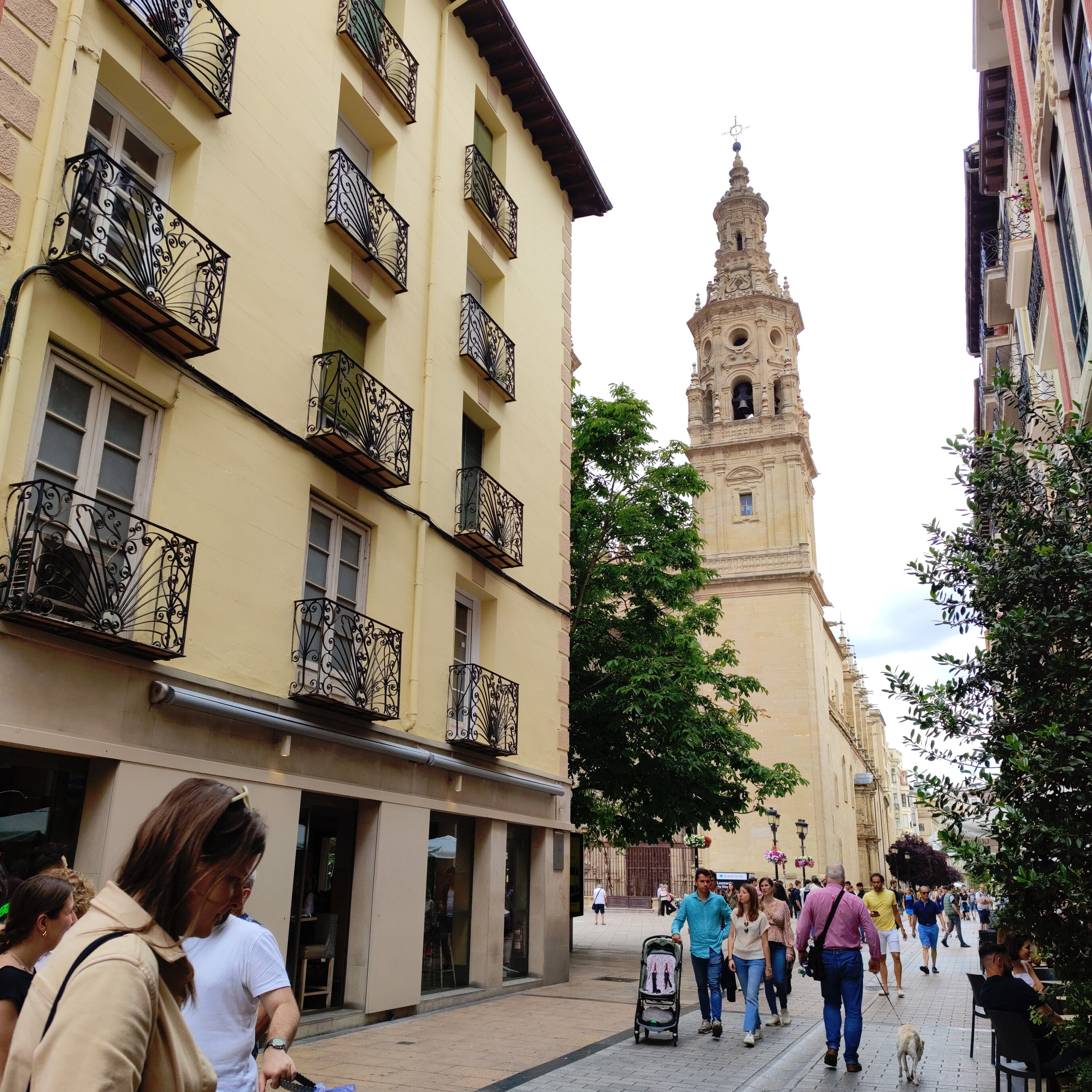 A street with buildings, a tower, and people walking.
