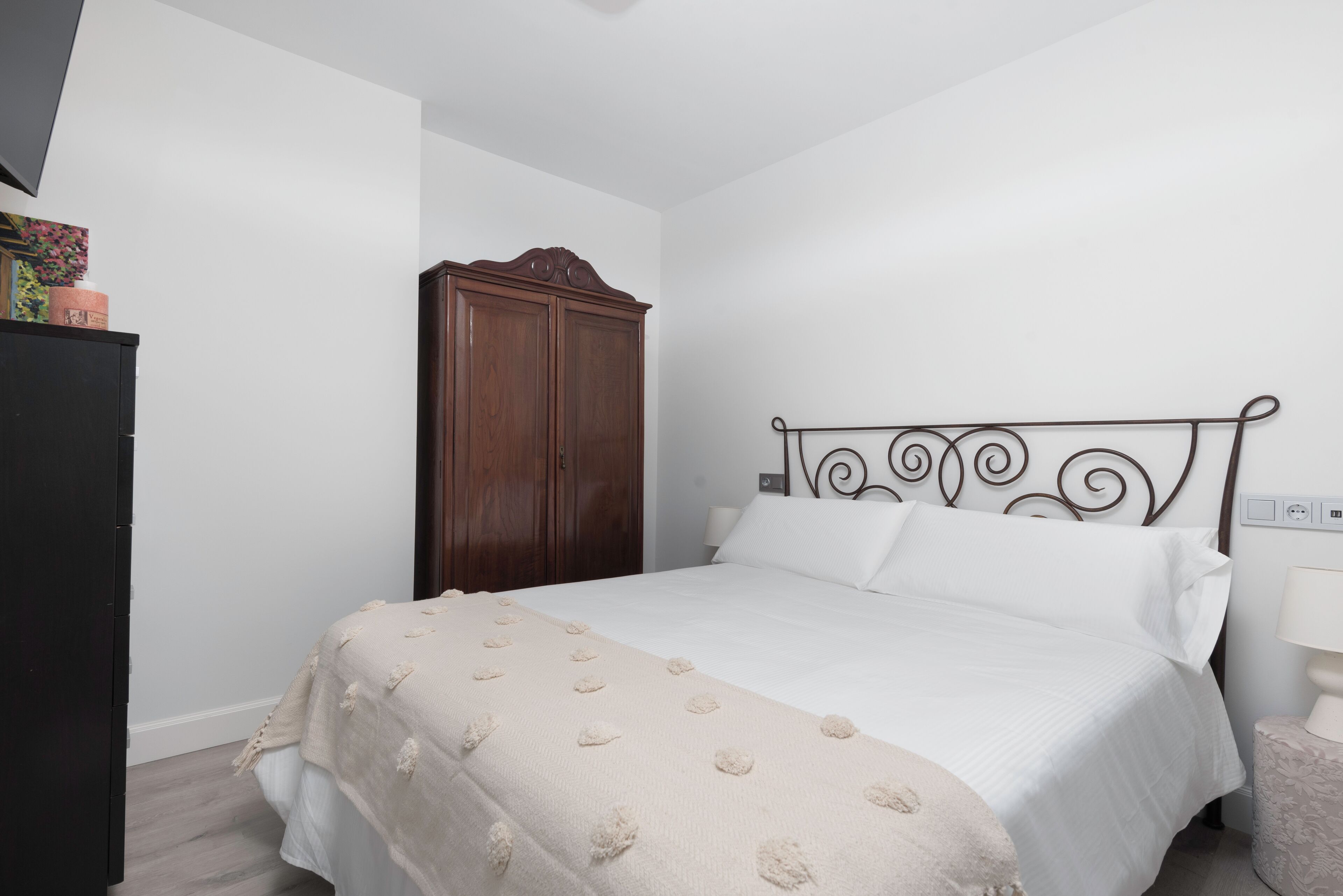 Een slaapkamer met een bed, een houten garderobe en een nachtkastje met een lamp.