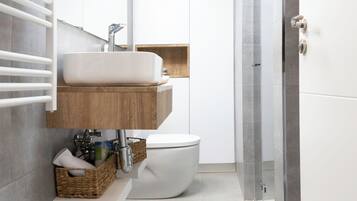 Een moderne badkamer met een wit wastafelmeubel, een houten opbergkast en een douchecabine met glazen wanden.