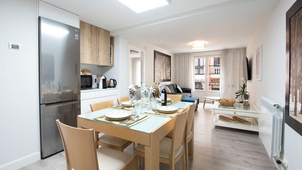 Une cuisine moderne dotée d’un réfrigérateur encastré, de meubles de rangement en bois et d’un coin repas avec une table dressée pour quatre personnes.
