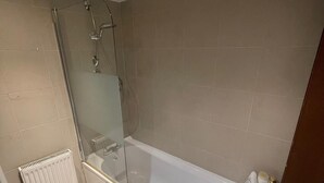 Une salle de bain avec une douche à parois de verre, une baignoire blanche et un radiateur.