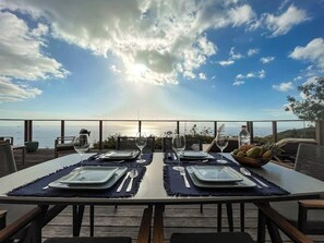 A dining table set for two with a view of the sea and sky.