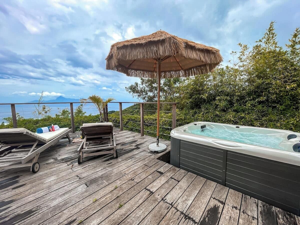 A wooden deck with lounge chairs, a hot tub, and a thatched umbrella.
