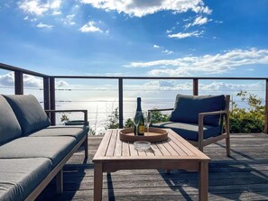 Una terraza de madera con un sofá y dos sillones, una botella de champán y dos copas sobre una bandeja.