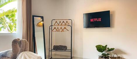 Una habitación con cama, televisión, espejo, perchero y plantas en macetas.