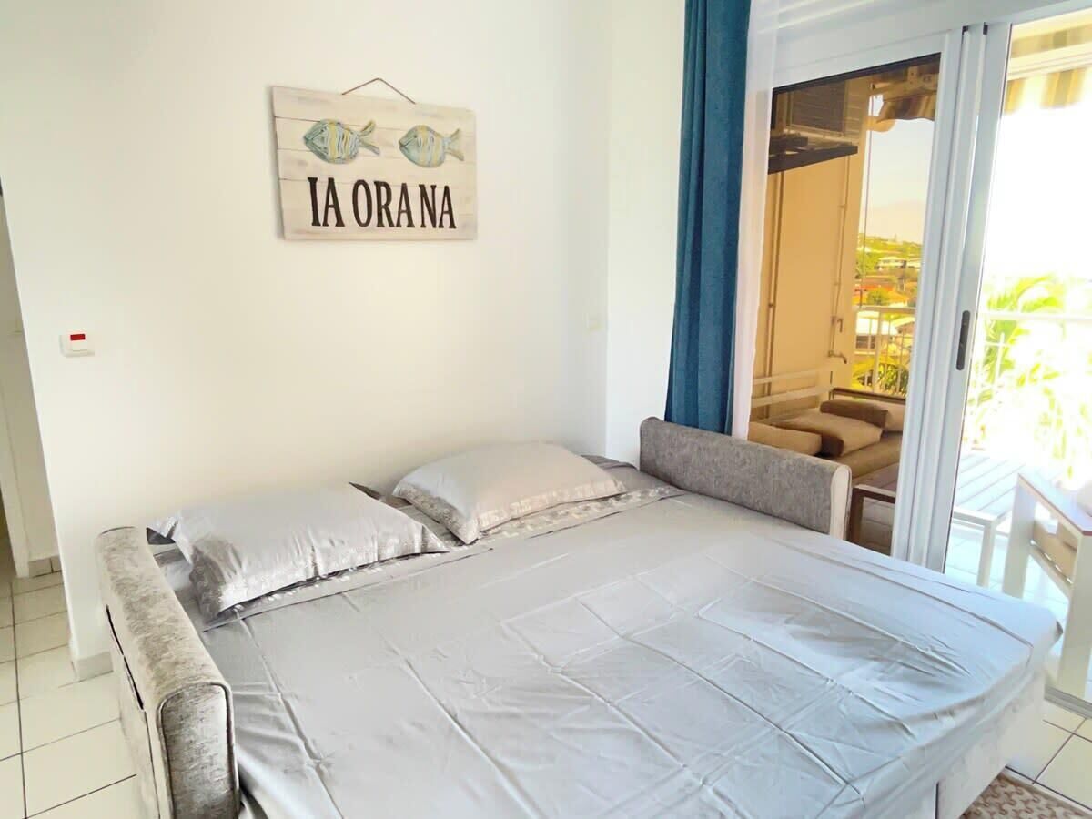 Un dormitorio con cama, almohadas, un cartel en la pared y vistas a un balcón con una silla.