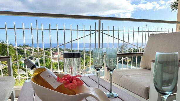 Ein Tisch mit einer Weinflasche, einer Blume und zwei Gläsern auf einem Balkon mit Blick auf eine schöne Aussicht.