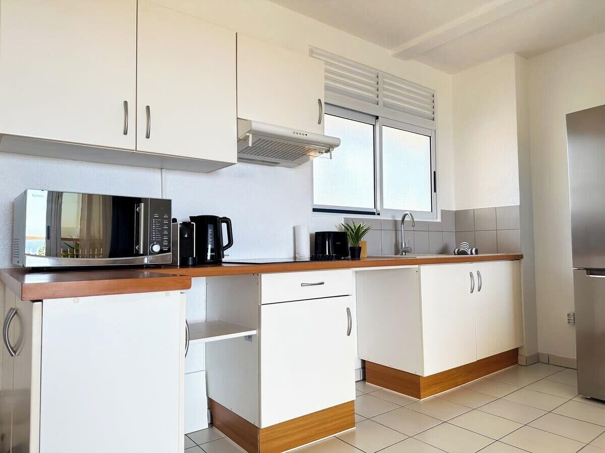 A modern kitchen with white cabinets, a stainless steel refrigerator, a microwave, and a coffee maker.